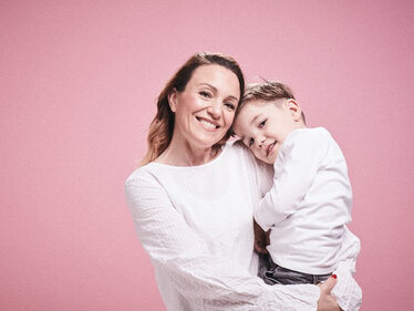 Woman holding her child in front of a pink background