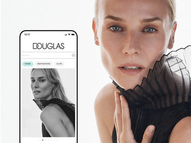 Smartphone mit DOUGLAS App neben einem Porträt von Botschafterin Diane Krüger